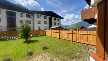 Grüner Gartenbereich mit Rasenfläche, Holzzaun und Bergblick im Hintergrund.