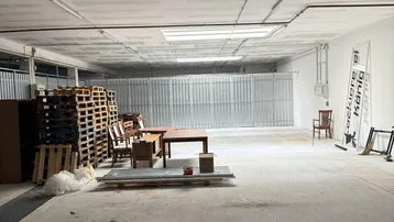 Großer, leerer Lagerraum mit Betonboden, gestapelten Paletten und sichtbaren Installationen an der Decke.