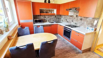Moderne Einbauküche in Orange mit Essbereich und Fenster, ausgestattet mit Elektrogeräten.