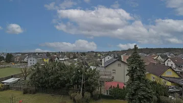 Weitläufiger Blick über eine Wohnsiedlung mit vielen Bäumen und Häusern unter einem bewölkten Himmel.