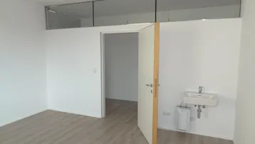 Heller Büroraum mit Laminatboden, einer kleinen Spüle und einer Glastrennwand im oberen Bereich.