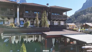 Traditionelles Gebäude mit Holzbalkonen und Glasanbau, umgeben von einer malerischen Berglandschaft.