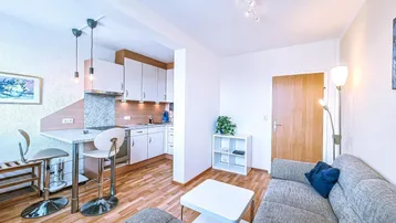Helles Wohnzimmer mit offener Küche, Parkettboden und gemütlichem Sofa in einem kombinierten Bereich.