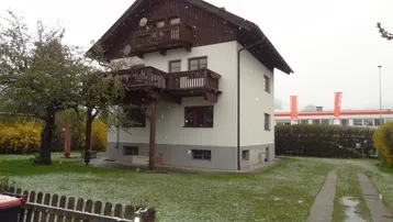 Freistehendes Haus mit weißer Fassade, Holzbalkonen und Garten, leicht mit Schnee bedeckt.