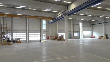 Geräumige Lagerhalle mit hohen Decken, Oberlichtern und mehreren Rolltoren für den Zugang.