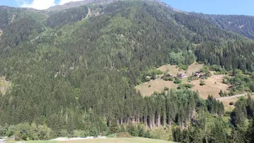 Panoramablick auf bewaldete Berge mit vereinzelten Häusern in der Ferne unter blauem Himmel.