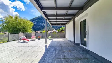 Geräumige, überdachte Terrasse mit Fliesenboden und Zugang zum Innenbereich, umgeben von Natur.