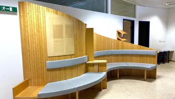 Geschwungene Sitzbank mit Holzvertäfelung und Polstern in einem Wartebereich.