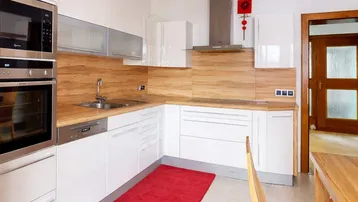 Moderne Küche mit weißen Hochglanzfronten, Holzakzenten und integrierten Geräten, inklusive Backofen und Mikrowelle.