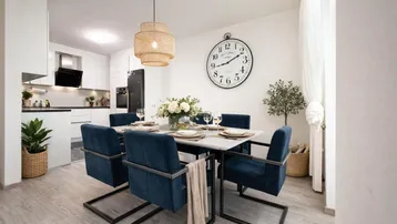 Helles Esszimmer mit modernem Esstisch, blauen Stühlen und offener Küche im Hintergrund.