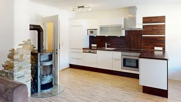 Offene Küche mit weißen Schränken, Holzboden und einem modernen Holzofen.