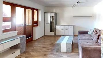 Geräumiges Wohnzimmer mit Holzboden, bequemer Couch und Zugang zu einem Außenbereich.