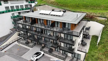 Moderne Wohnanlage mit Balkonen, Terrassen und Solaranlagen auf dem Dach in grüner Umgebung.