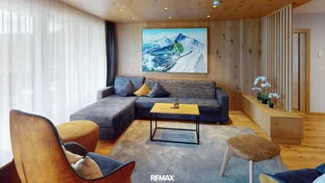 Gemütliches Wohnzimmer im alpinen Stil mit Holzwänden, bequemer Couch und Bergbild.