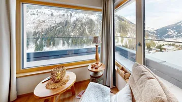 Gemütlicher Wohnbereich mit großen Fenstern und atemberaubendem Blick auf die verschneiten Berge.