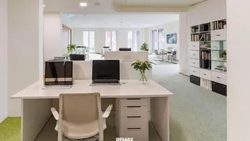Modernes Büro mit mehreren Arbeitsplätzen, hellen Wänden und Teppichboden in einem offenen Grundriss.