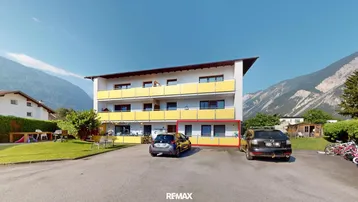 Mehrfamilienhaus mit gelben Balkonen und Bergblick in ländlicher Umgebung.