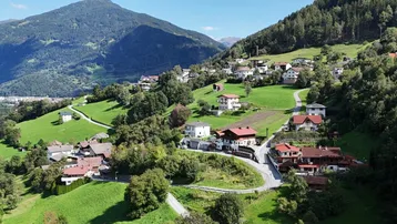 Luftaufnahme eines malerischen Dorfes in einer grünen Berglandschaft mit vielen Häusern.