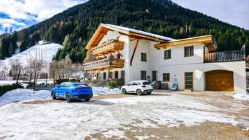 Großes Haus in den Bergen mit verschneiter Landschaft und zwei Autos auf dem Vorplatz.