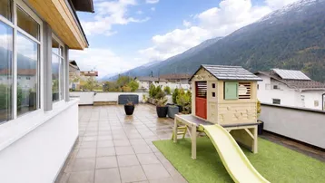 Geräumige Dachterrasse mit Spielhaus, Fliesenboden und beeindruckendem Bergblick auf die Berge.