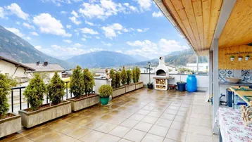 Großzügige Dachterrasse mit Grillplatz, Fliesenboden und weitem Bergblick in die Landschaft.