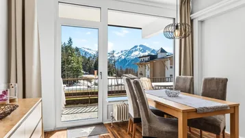 Heller Essbereich mit Holzboden, modernen Möbeln und direktem Zugang zum Balkon mit Bergblick.