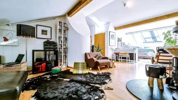 Geräumiges Wohnzimmer mit Holzboden, sichtbaren Holzbalken und großem Dachfenster, das viel Licht spendet.