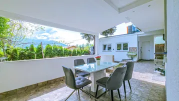 Überdachte Terrasse mit Esstisch und Stühlen, bietet einen schönen Bergblick und Fliesenboden.