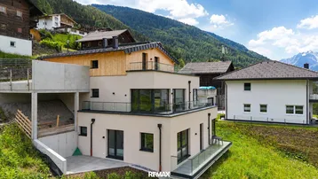 Modernes Wohnhaus in Hanglage mit mehreren Balkonen und Bergblick in alpiner Umgebung.
