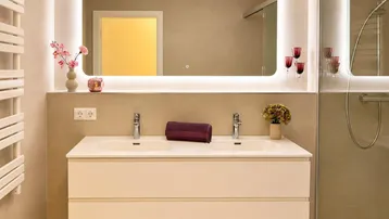 Modernes Badezimmer mit Doppelwaschbecken, beleuchtetem Spiegel und einer geräumigen begehbaren Dusche.