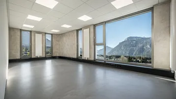 Geräumiger, leerer Büroraum mit großen Fenstern, die einen weiten Blick auf die Berge bieten.