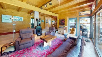 Gemütliches Wohnzimmer mit Holzbalkendecke, Kaminofen und großen Fenstern zum Garten.