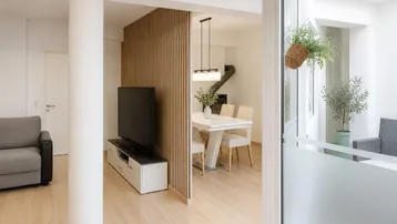 Helles Wohn- und Esszimmer mit Holzwandelementen und modernem Kaminofen.