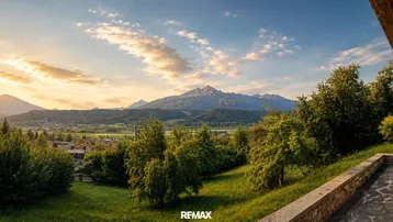 Panoramablick auf die Berge bei Sonnenuntergang von einer Terrasse mit viel Grün und warmem Licht.