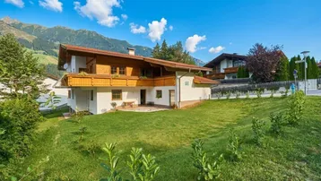 Traditionelles Haus im alpinen Stil mit Holzbalkonen und Bergblick unter blauem Himmel.