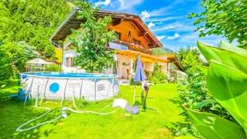 Großzügiger Gartenbereich mit Aufstellpool, umgeben von grüner Natur und Bergen.