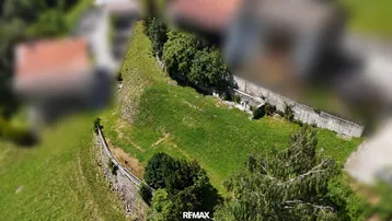 Luftaufnahme eines grünen, hügeligen Grundstücks mit Bäumen und Stützmauern in ländlicher Umgebung.