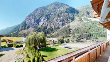 Geräumiger Holzbalkon mit weitem Blick auf die umliegende Berglandschaft und einen Spielplatz.