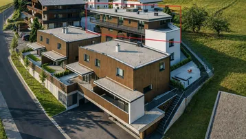 Moderne Wohngebäude in einer grünen Hügellandschaft mit umliegenden Bergen und viel Natur.
