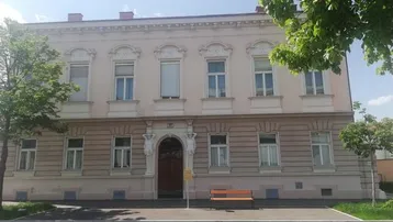 Klassisches Gebäude mit eleganter Fassade, verzierten Fenstern und einem kleinen Vorgarten.