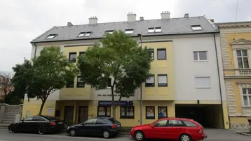Mehrfamilienhaus mit gelber Fassade, Dachfenstern und geparkten Autos auf der Straße.