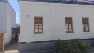 Gut erhaltenes Altbaugebäude mit weißer Fassade, dekorativen Elementen, Holzfenstern und Satteldach mit Dachfenstern.