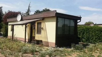 Kleines, einstöckiges Haus mit gelber Fassade und braunem Anbau, umgeben von einem naturbelassenen Garten.