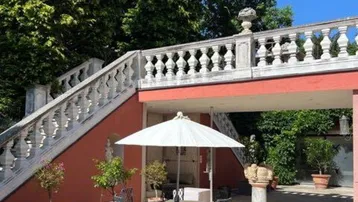 Große Steinterrasse mit Gartenmöbeln und Sonnenschirm, umgeben von üppigem Grün und einer eleganten Balustrade.