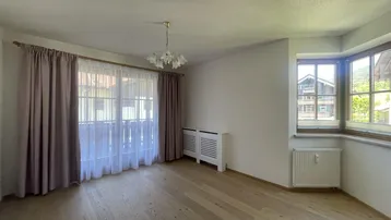 Geräumiges Zimmer mit Holzboden, großen Fenstern und Zugang zu einem französischen Balkon.