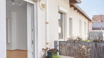 Heller Balkon mit Fliesenboden, Pflanzen und Zugang zu einem Innenraum mit Parkett.