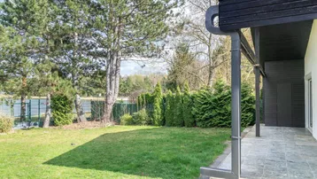 Gepflegter Gartenbereich mit Rasenfläche, hohen Bäumen und einer überdachten Terrasse am Haus.