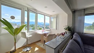 Heller Wohn- und Essbereich mit großen Fenstern, Panoramablick auf Berge und Stadt sowie modernem Interieur.