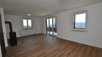 Helles Wohnzimmer mit Holzboden, gemütlichem Holzofen und Zugang zu einem Balkon mit Aussicht.