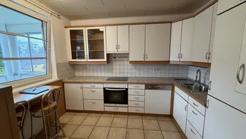 Funktionale Küche mit weißen Schränken, Fliesenboden und integrierten Geräten.